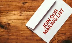 Join our mailing list imprint stamp on white paper envelope placed on top of office desk, top view