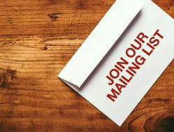 Join our mailing list imprint stamp on white paper envelope placed on top of office desk, top view